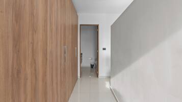 A hallway with a wooden wardrobe, a white wall, and a door leading to a bathroom.