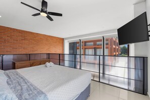 A modern bedroom with a large bed, a ceiling fan, a brick wall, and a balcony with a view of buildings. - Zoho Skies by Monyxbnb (Puerto Vallarta)