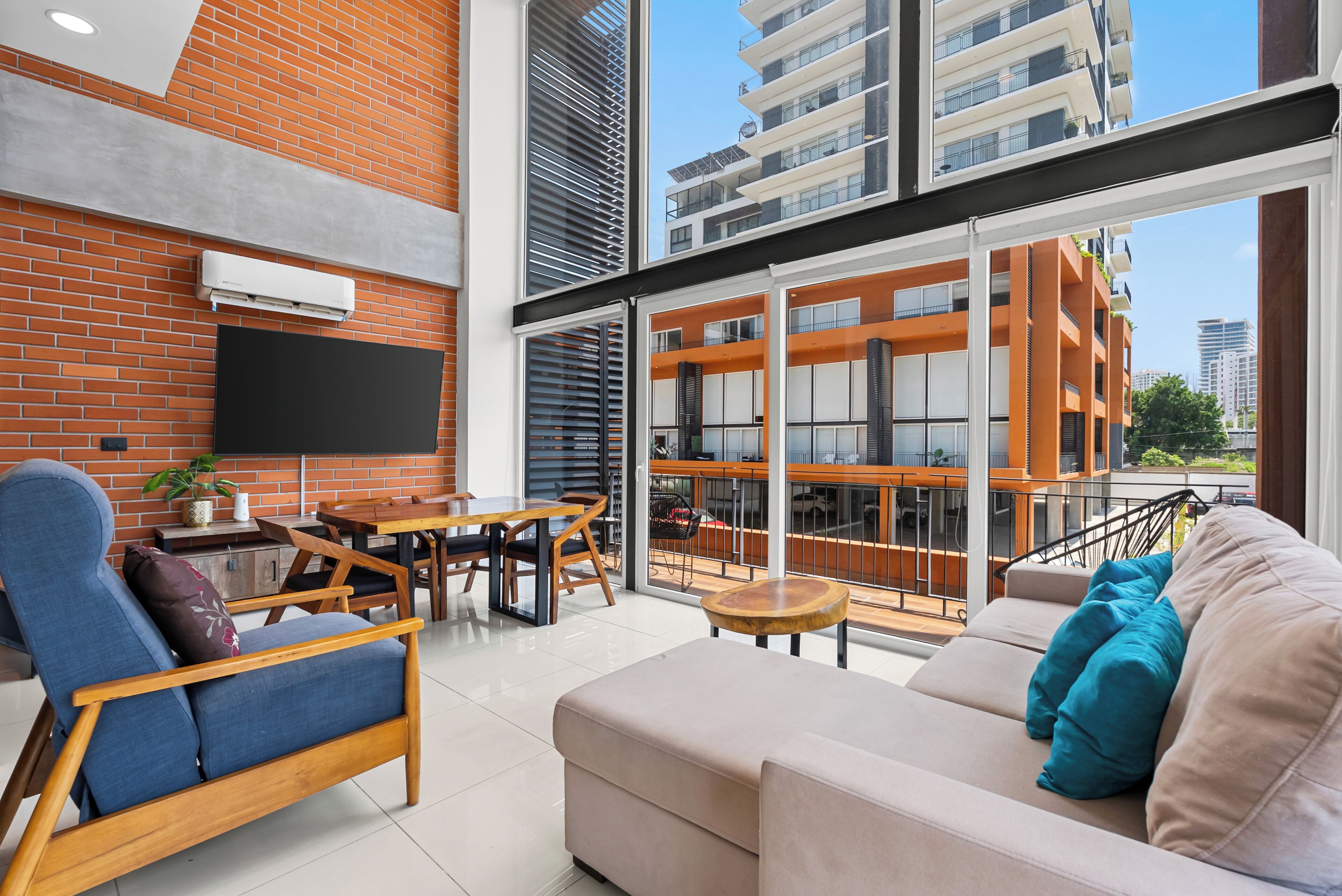 A modern living room with a brick wall, a flat-screen TV, a sofa, and a dining area with a table and chairs.