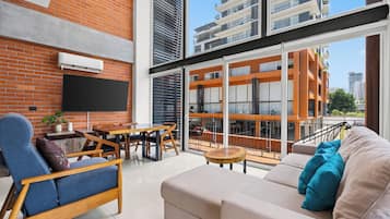 A modern living room with a brick wall, a flat-screen TV, a sofa, and a dining area with a table and chairs.