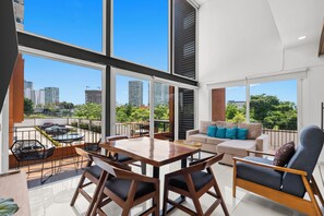 A modern living room with a large window, a dining area, and a sofa with blue cushions. - Zoho Skies by Monyxbnb (Puerto Vallarta)