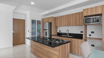 Une cuisine moderne avec des meubles en bois, un plan de travail noir, un four à micro-ondes encastré et un évier en acier inoxydable.