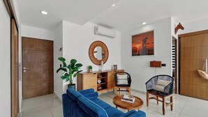 A modern living room with a blue sofa, a wooden cabinet, a round mirror, and a painting of a sunset. - Zoho Skies by Monyxbnb (Puerto Vallarta)