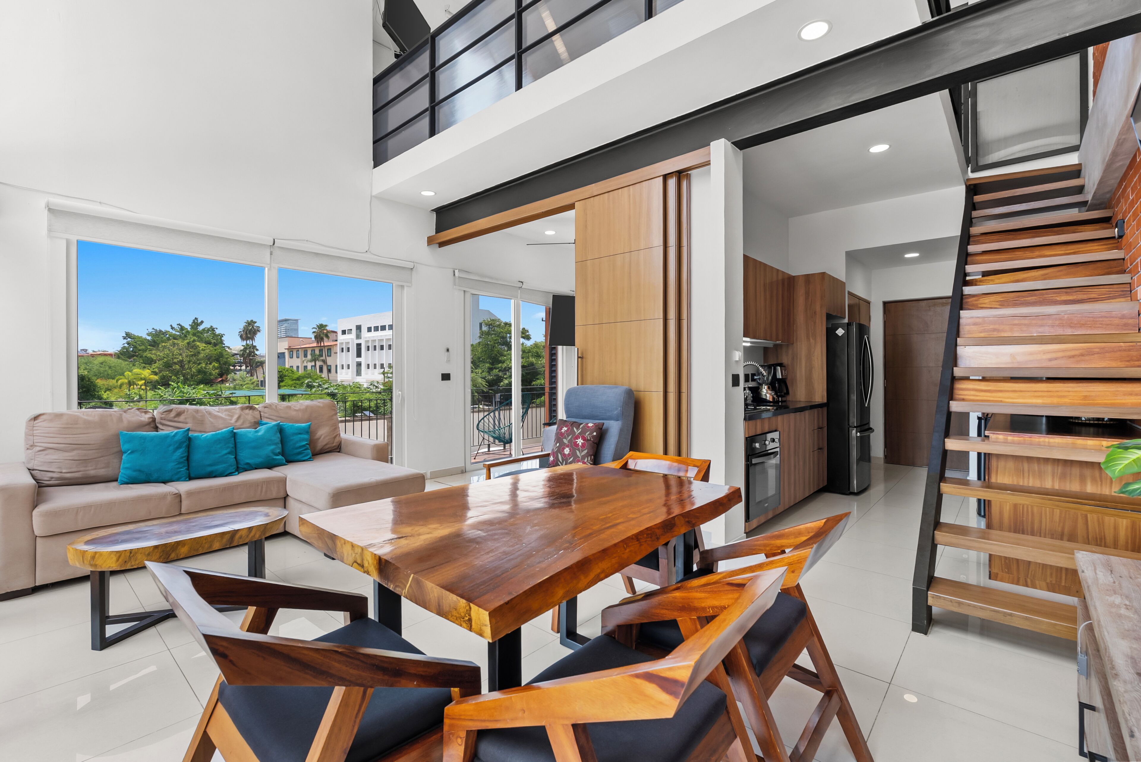 A modern interior with a dining area, sofa, kitchen, and a staircase.