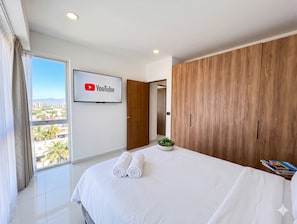 A modern hotel room with a large bed, a YouTube TV screen, a wooden wardrobe, and a view of the city. - Zoho Skies by Monyxbnb (Puerto Vallarta)