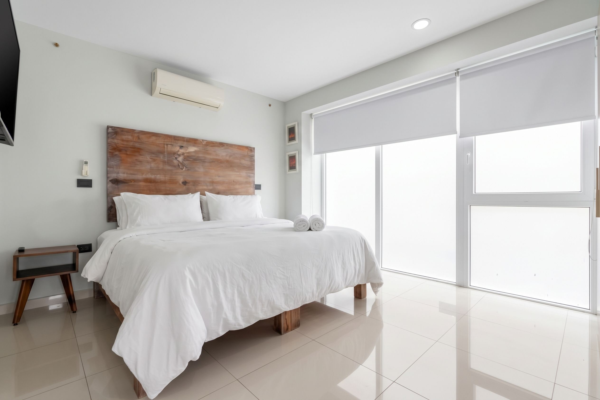 Une chambre à coucher moderne avec un grand lit, une tête de lit en bois, une table de chevet et un téléviseur fixé au mur.