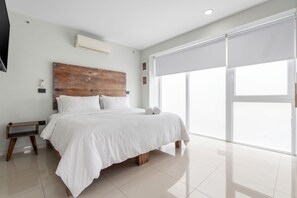 Un dormitorio moderno con una cama grande, cabecera de madera, mesita de noche y televisor montado en la pared.