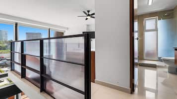 A modern interior with a view of the city through large windows, a ceiling fan, and a sliding glass door leading to a bathroom.