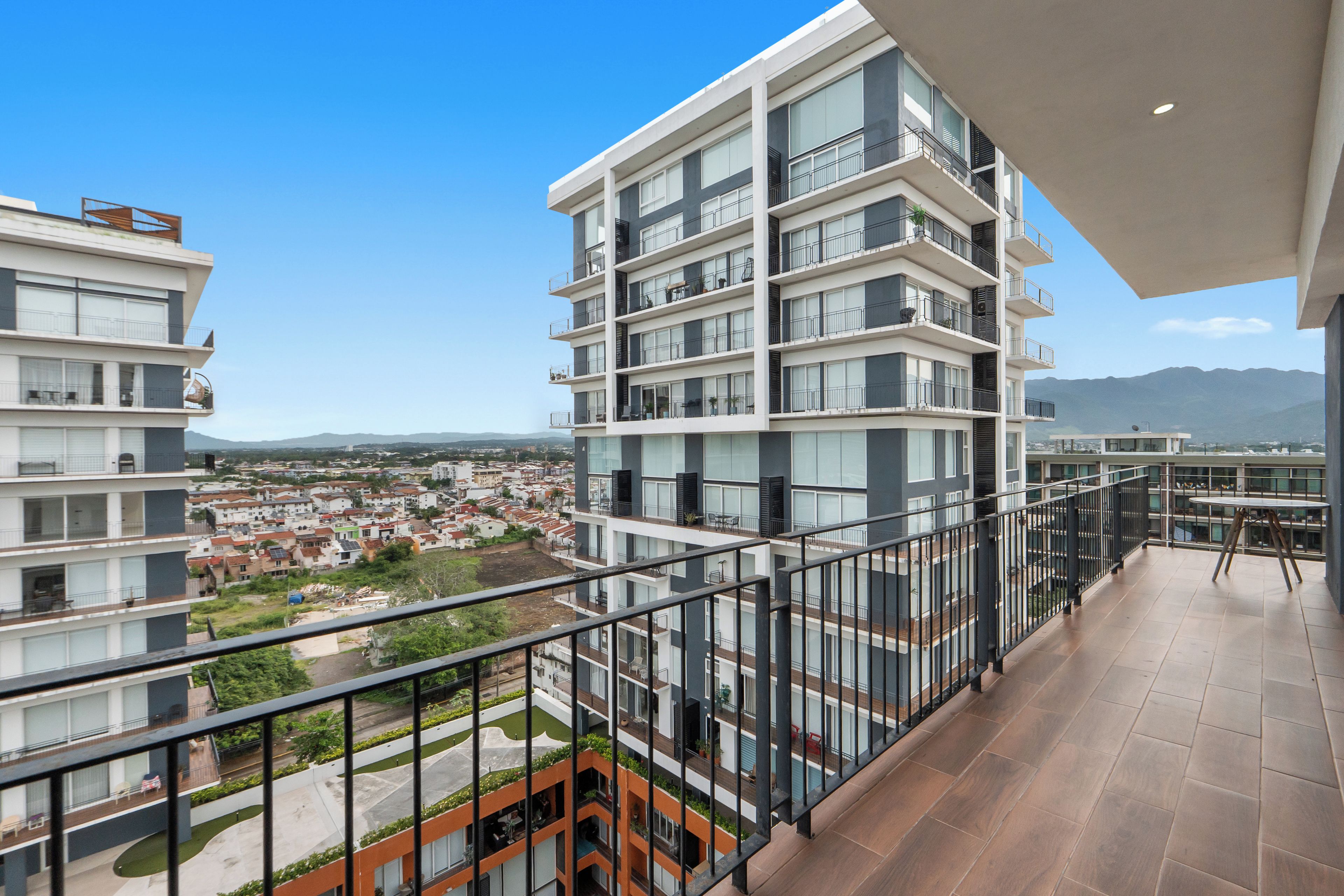 A multi-story residential building with balconies, a courtyard, and a view of a town and mountains in the distance.