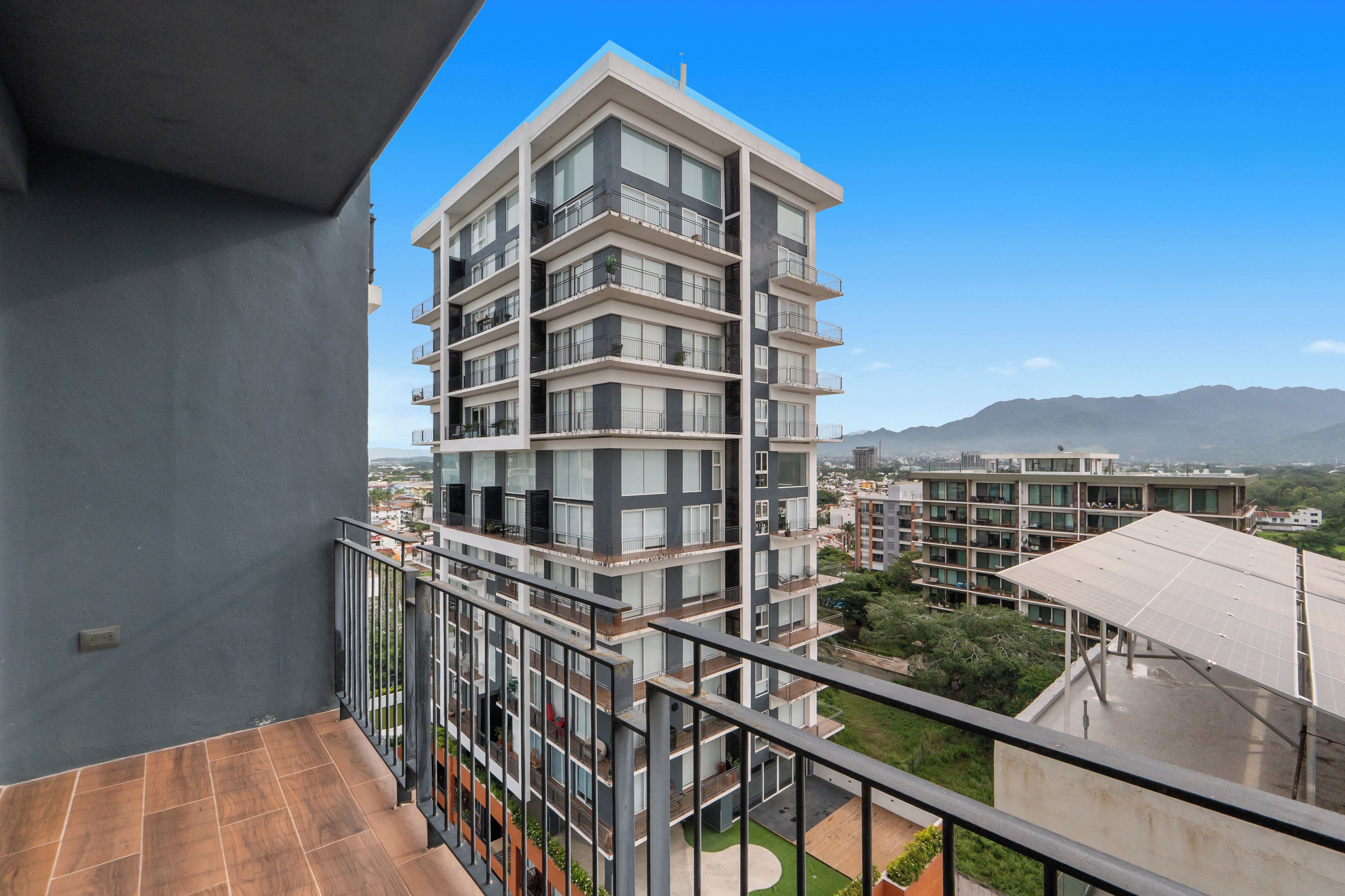 Un edificio residencial de varios pisos con balcones, vista de los alrededores y una montaña al fondo.