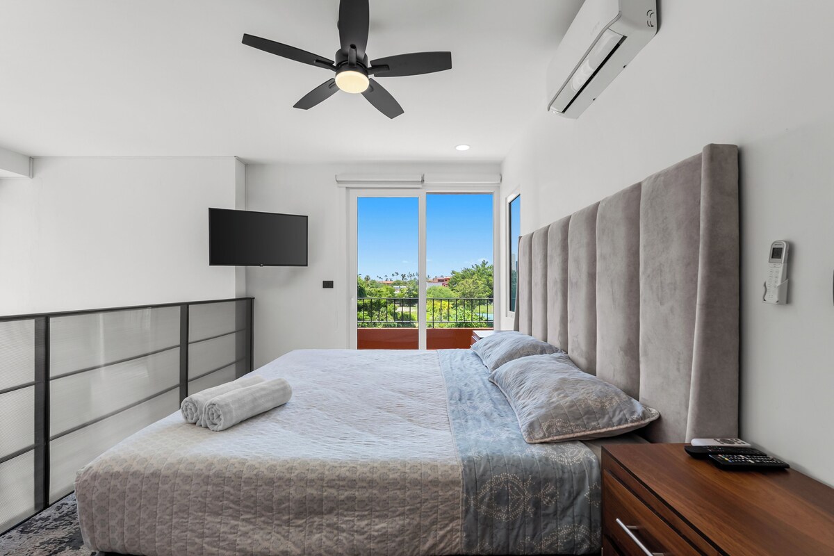 A bedroom with a bed, a TV, a ceiling fan, and an air conditioner.