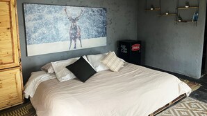 A bedroom with a bed, pillows, a wall-mounted artwork of a deer in a snowy landscape, a wooden cabinet, and a shelf with decorative items.