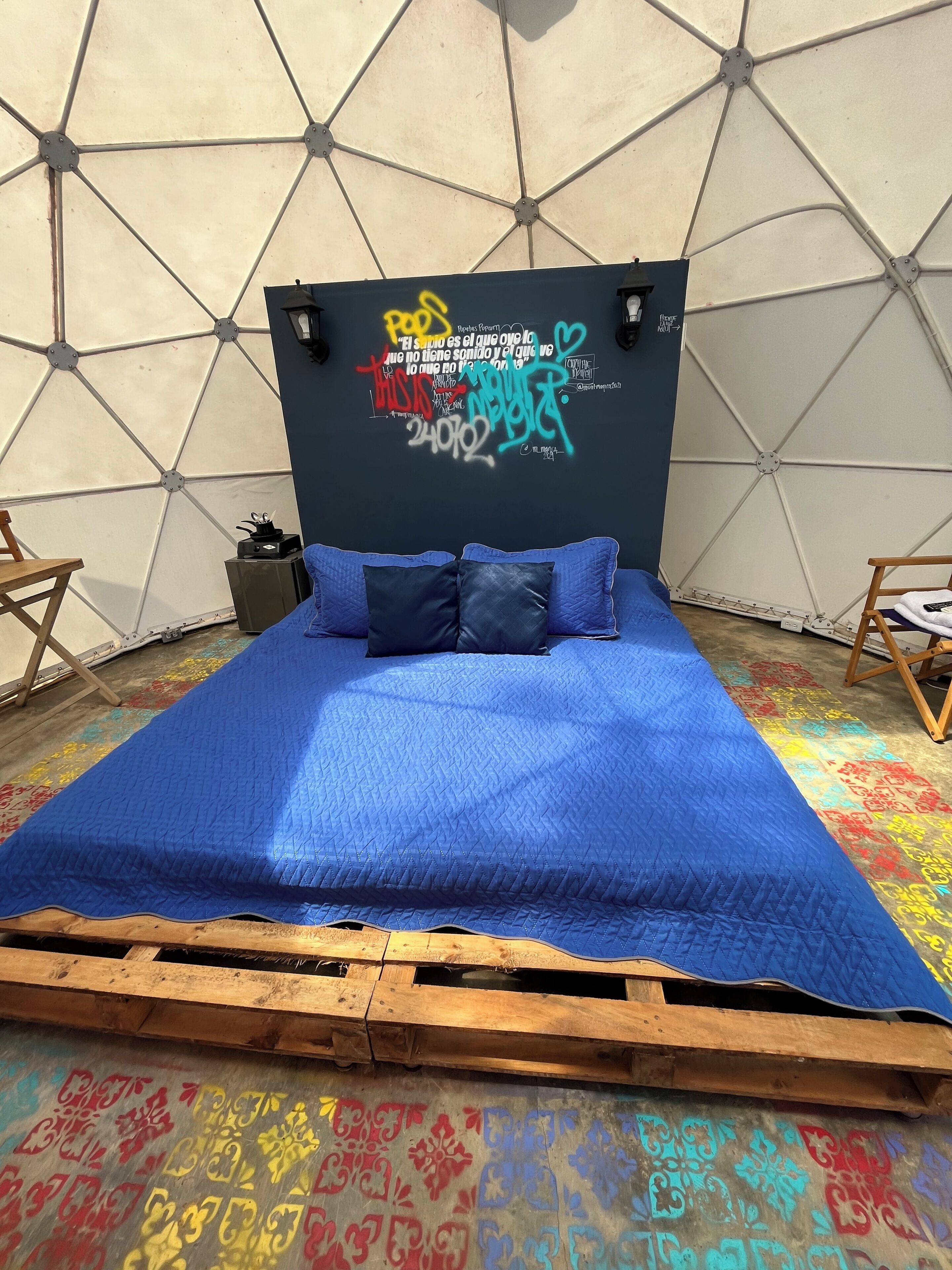 Ein Bett mit blauer Steppdecke, einer geometrischen Wand und einem Holzboden mit bunten Mustern.