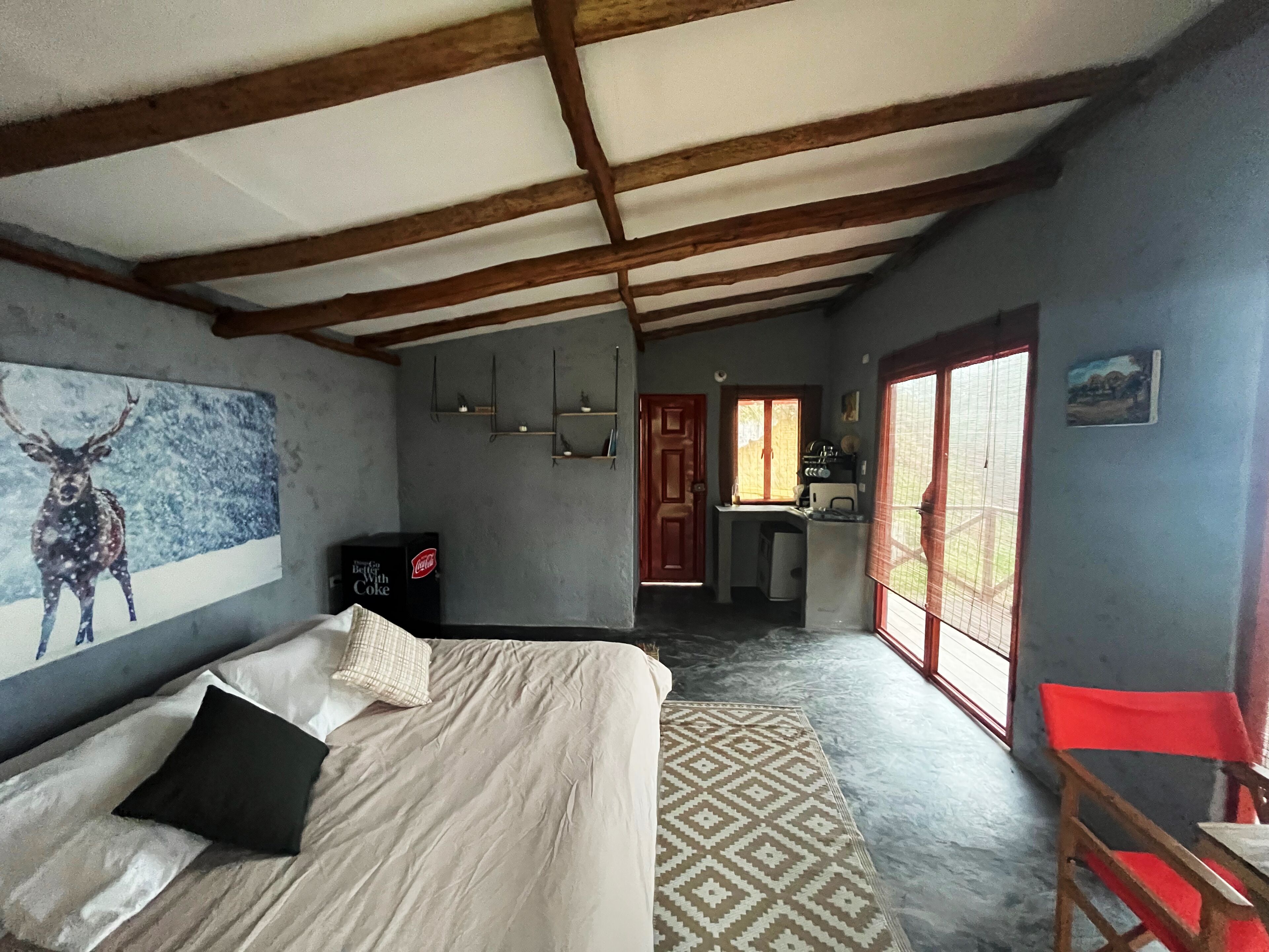 Un dormitorio con cama, un cuadro de un ciervo, un refrigerador, una ventana y una puerta que da a una zona de cocina.