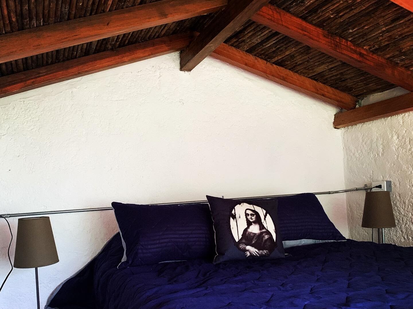 A bedroom with a wooden ceiling, a bed with dark blue bedding, and two wall-mounted lamps.
