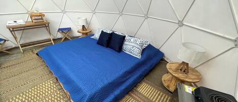 A room with a bed, a small desk, a chair, a lamp, and a heater.