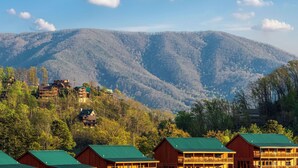 A mountain lodge with multiple wooden buildings, green roofs, and a backdrop of forested hills. - Beautiful Views, Spacious, Hot Tub, Easy Access Roads, & Free Attractions! (Sevierville)