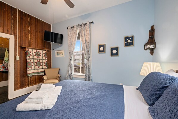 Een slaapkamer met een groot bed, een houten wand, een televisie en een raam met gordijnen.