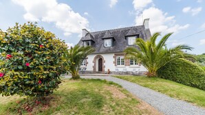 A house with a stone facade, a central archway, and a gravel driveway leading to the entrance.