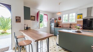 A modern kitchen with a wooden counter, bar stools, a refrigerator, and a large window.