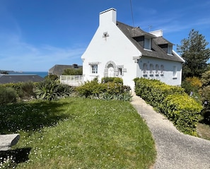 A white house with a sloped roof, a stone chimney, and a small window.