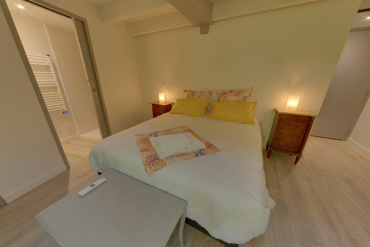 A bedroom with a bed, bedside tables, a nightstand, a small table, and a door leading to a bathroom.