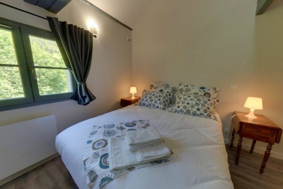 A neatly made bed with patterned bedding, two bedside lamps, and a window with curtains.