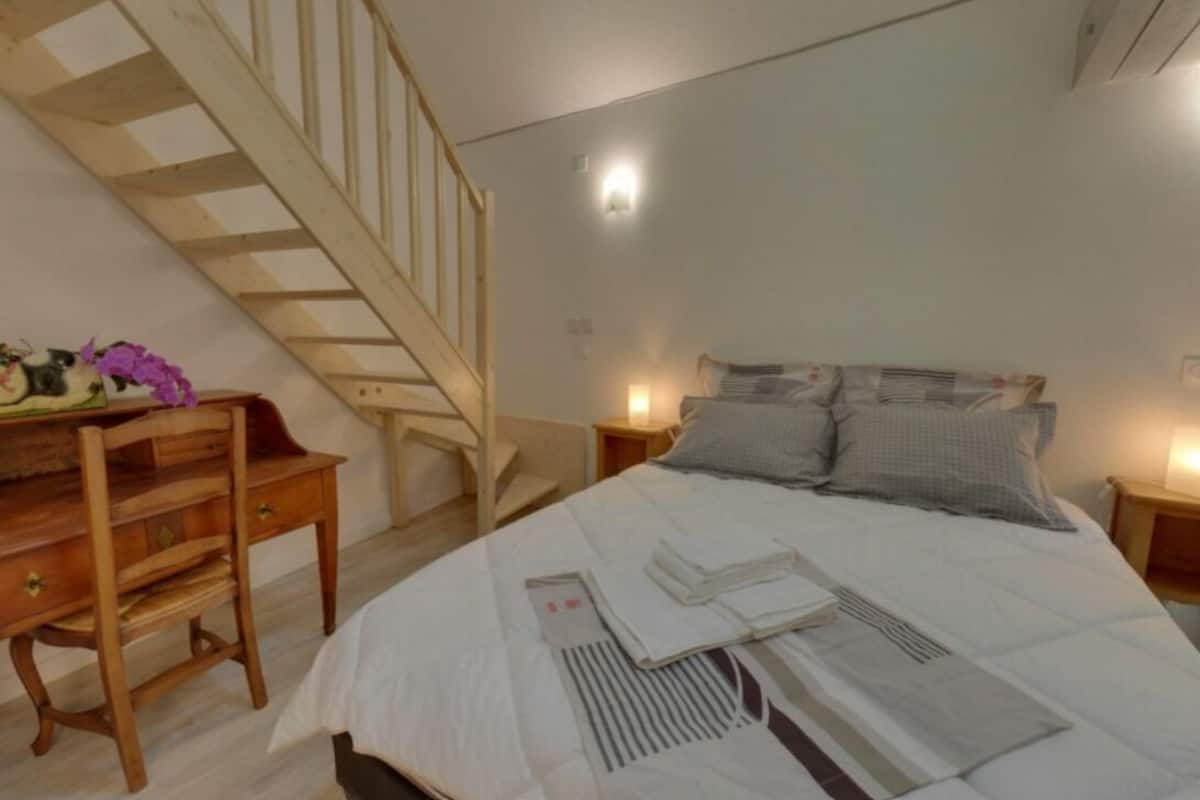 A bedroom with a wooden bed, a desk with a chair, a staircase, and bedside lamps.