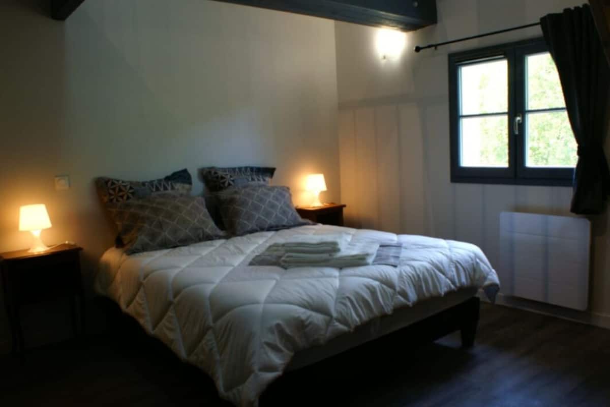 A bedroom with a bed, two bedside lamps, a window with curtains, and a radiator.