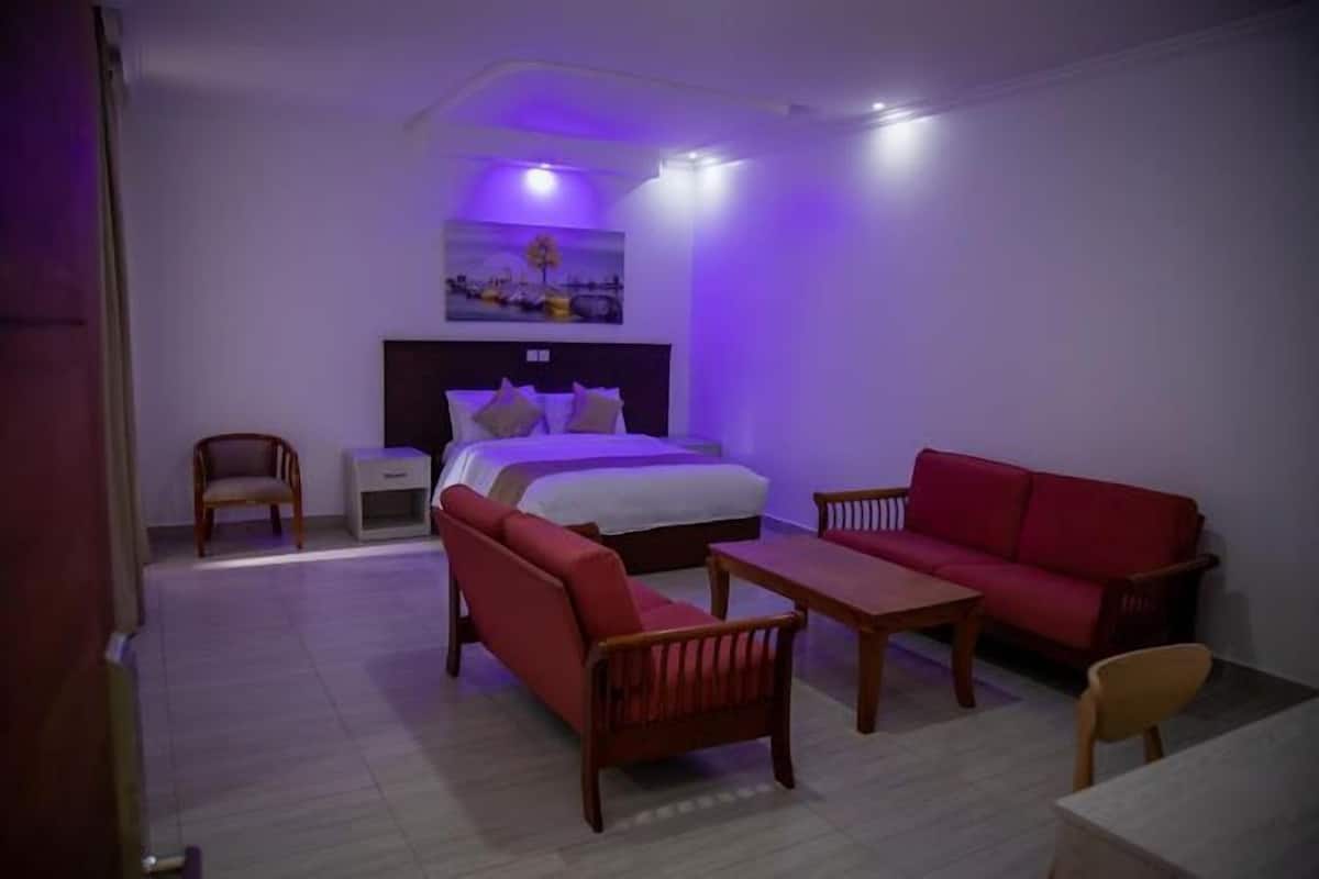 A hotel room with a bed, a red sofa, a wooden table, and a chair.