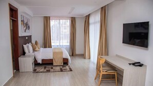 A hotel room with a bed, a desk, a chair, a TV, and a window with curtains. - Asumbi Resort  (Asumbi)