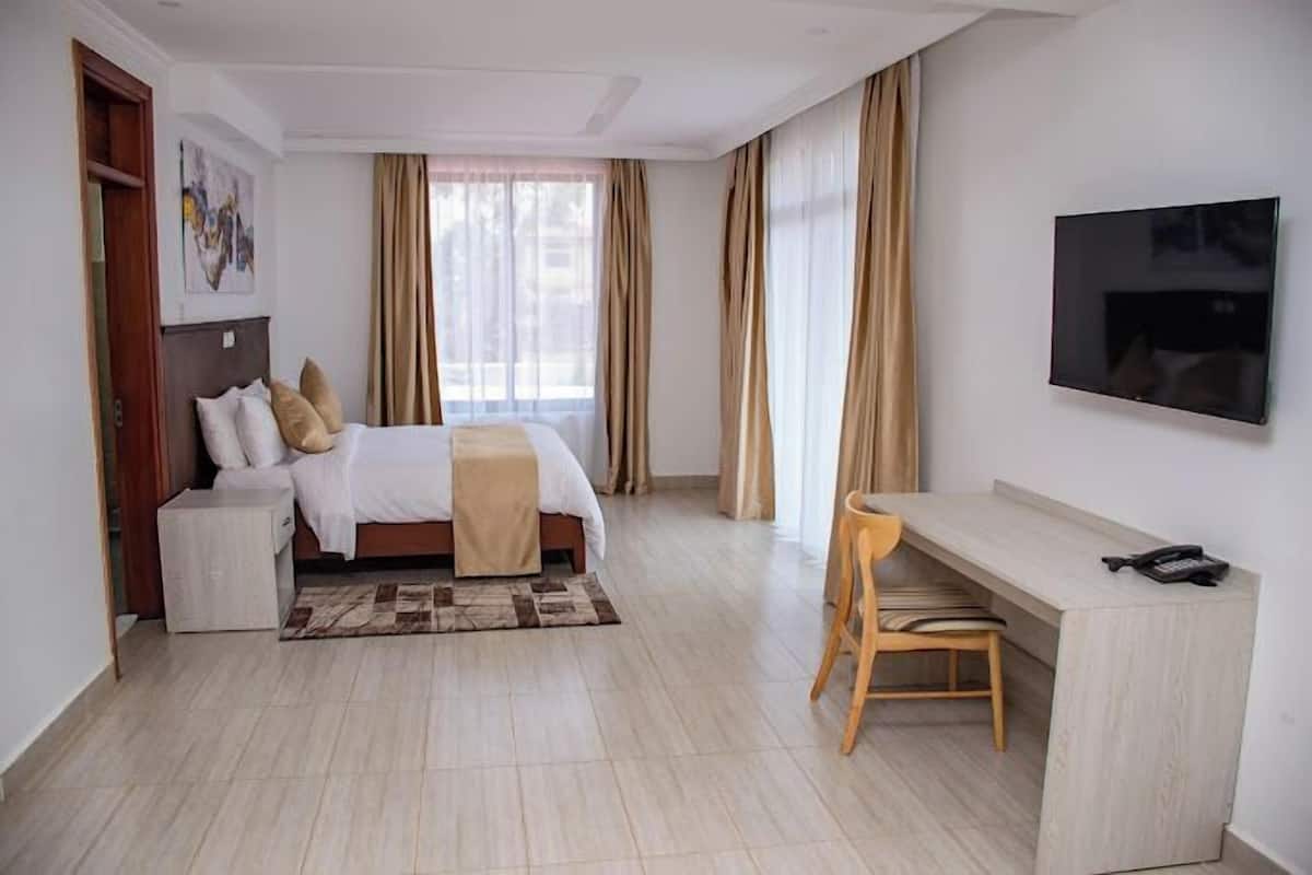 A hotel room with a bed, a desk, a chair, a TV, and a window with curtains.