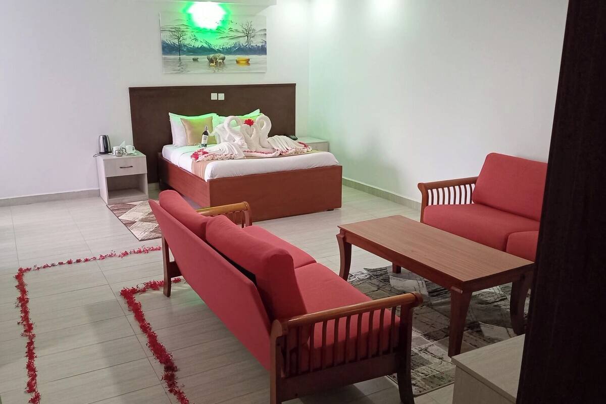 A hotel room with a bed, a red sofa, a wooden table, and a nightstand.
