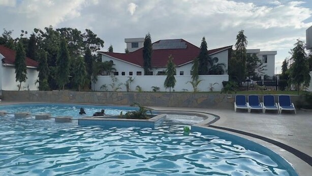 A swimming pool with a stone border, surrounded by lounge chairs and a building with a red roof. - Asumbi Resort  (Asumbi)