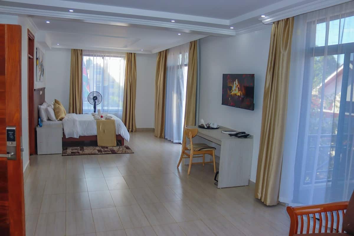 A hotel room with a bed, desk, chair, and large windows with curtains.