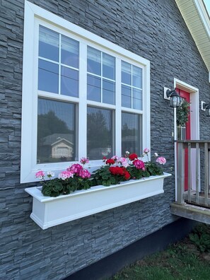 A building with a large window, stone facade, and a flower box with pink and red flowers.