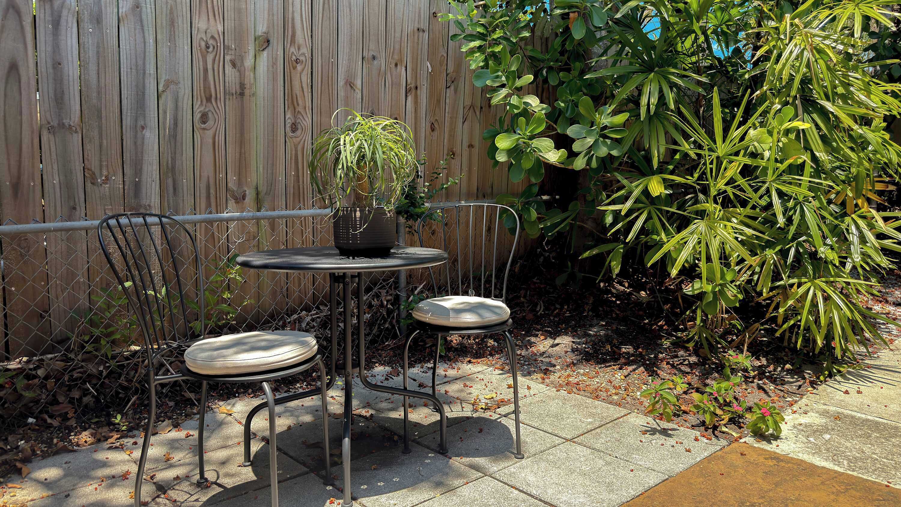 A metal outdoor table and two chairs with a potted plant on the table.