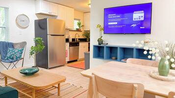 A modern kitchen with a refrigerator, sink, and cabinets, a dining area with a table and chairs, and a TV displaying a welcome message.