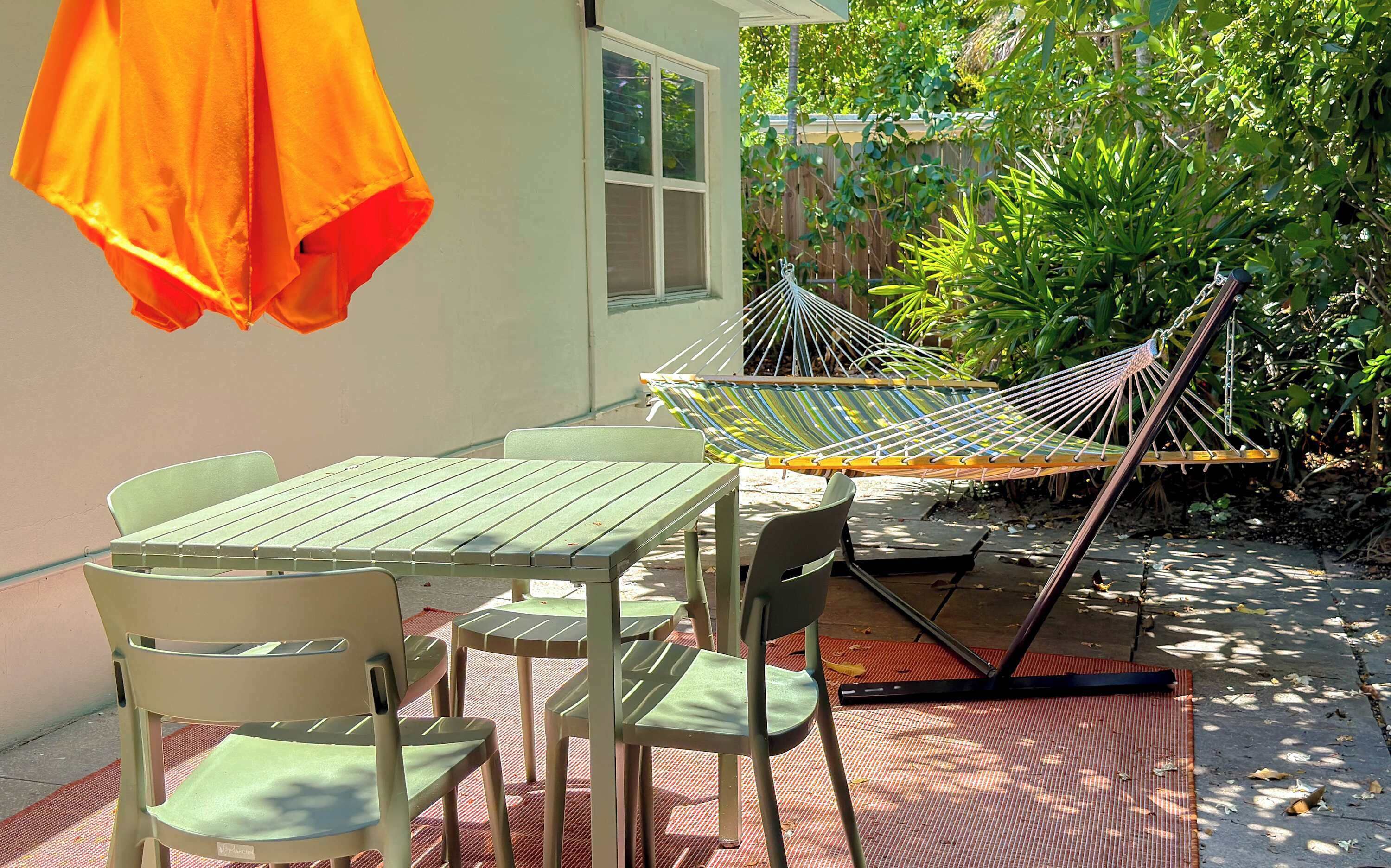 A patio with a table and chairs, a hammock, and a hanging orange cloth.