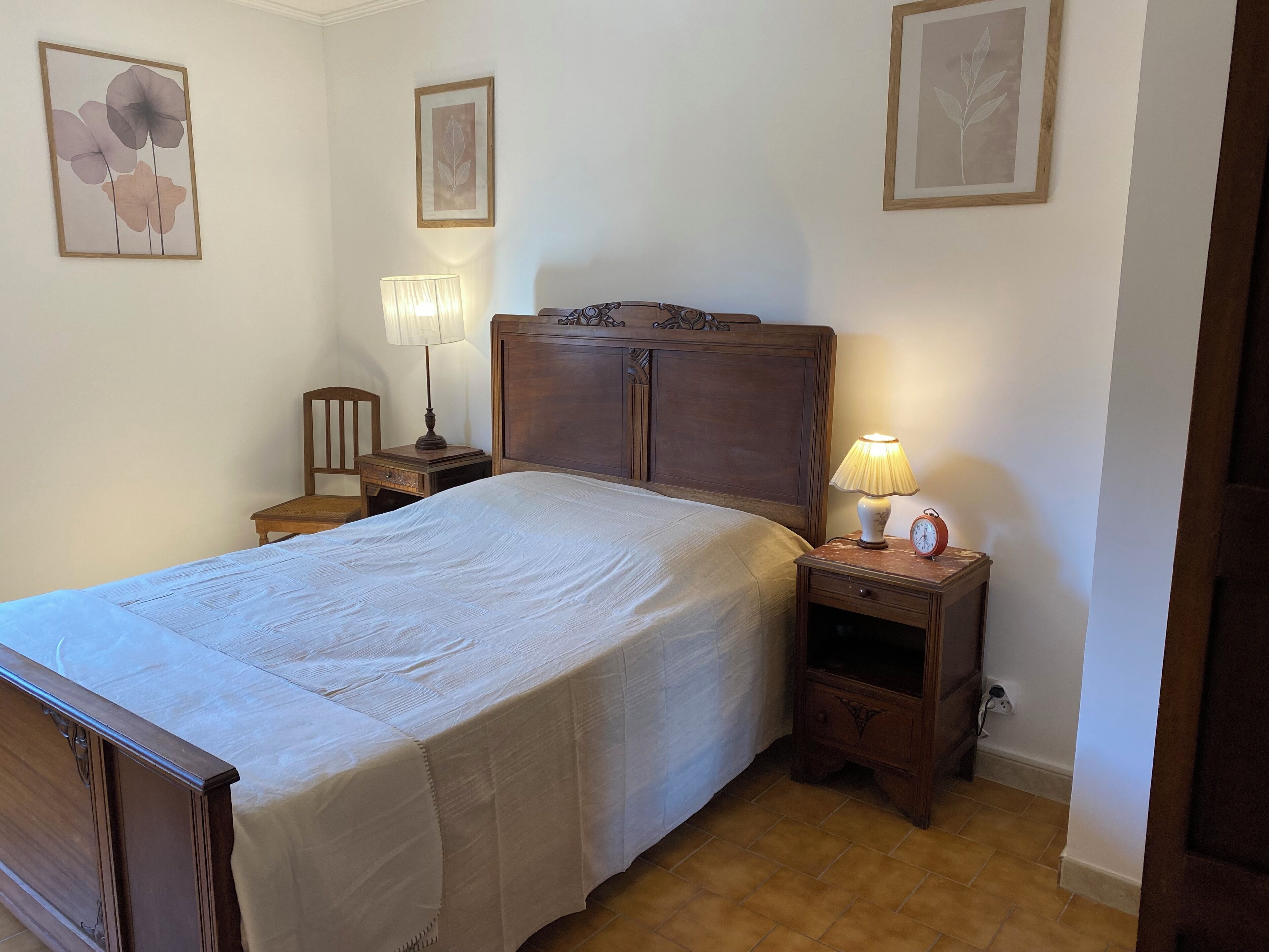 A neatly made bed with a wooden headboard, two bedside tables with lamps, and a nightstand with a clock.