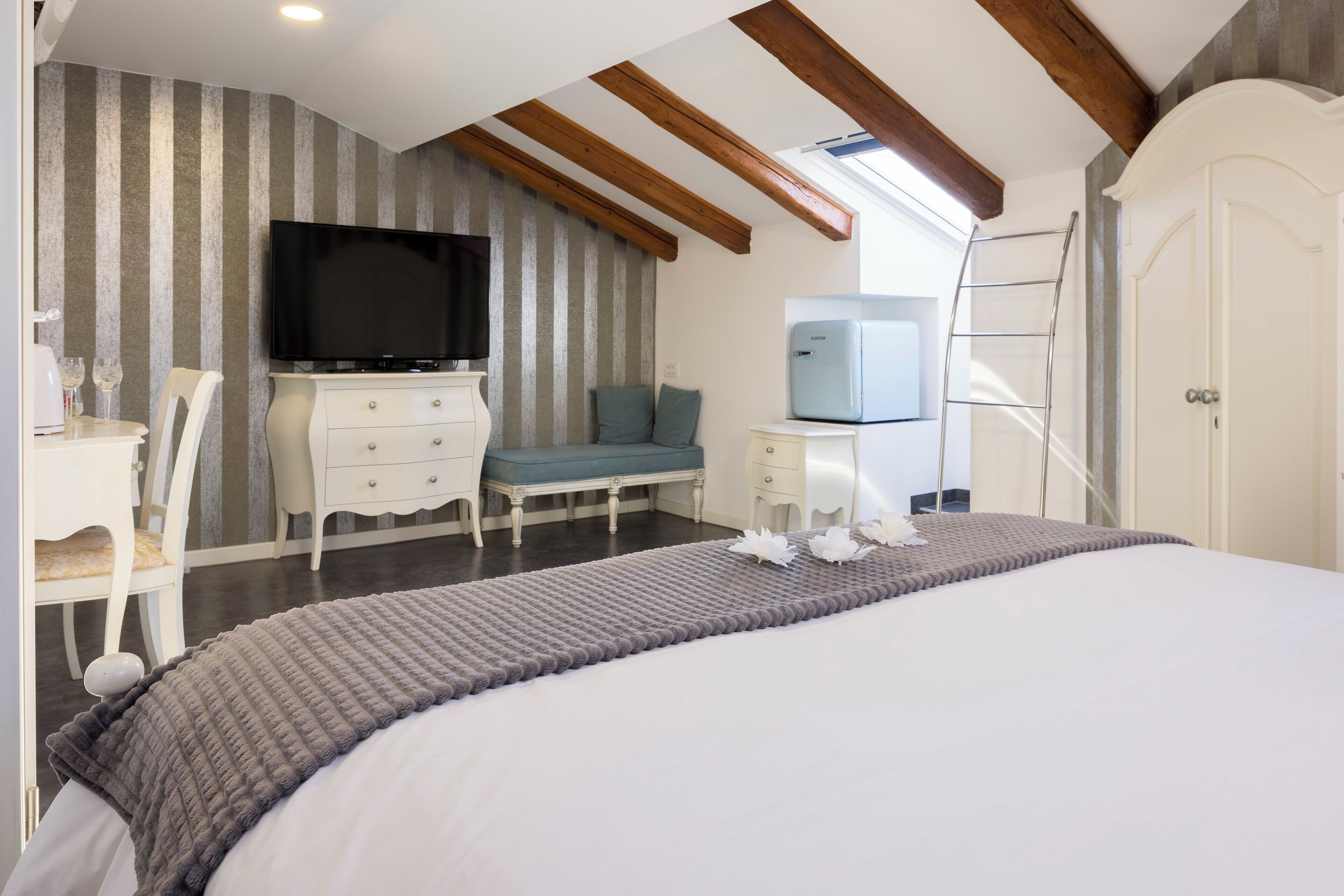 A bedroom with a bed, a TV, a dresser, a chair, a sofa, a ladder, and a wardrobe.