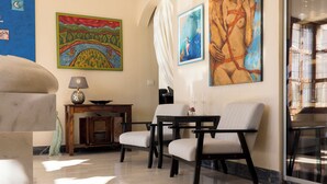 Une pièce comprenant un canapé, deux fauteuils, une petite table avec une lampe et des œuvres d’art accrochées aux murs.