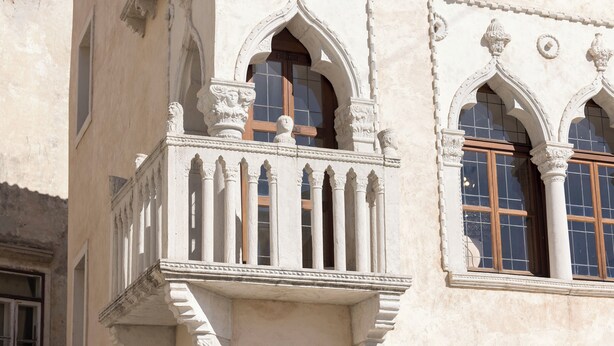 Une façade d’immeuble ornée de détails architecturaux raffinés, notamment un balcon avec des colonnes et une fenêtre avec un cadre en bois.