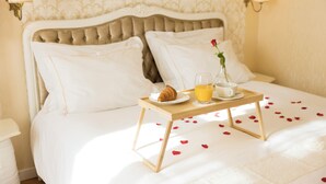 Un lit bien fait, sur lequel se trouve un plateau avec divers éléments pour le petit-déjeuner, notamment un croissant, une tasse et un verre de jus d’orange, le tout posé sur un présentoir en bois.