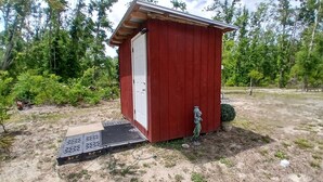 Un cobertizo de madera roja con una puerta blanca, un escalón pequeño que lleva a él y una manguera de jardín conectada al lateral.