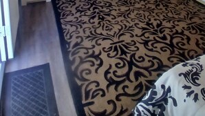 Una habitación con techo de madera, un escritorio con silla, un mueble pequeño y una alfombra estampada.