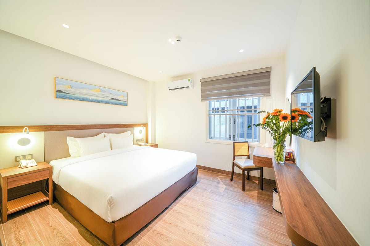 Une chambre d’hôtel avec un grand lit, des tables de chevet avec des lampes, un bureau avec une chaise, une fenêtre avec des stores et un téléviseur fixé au mur.