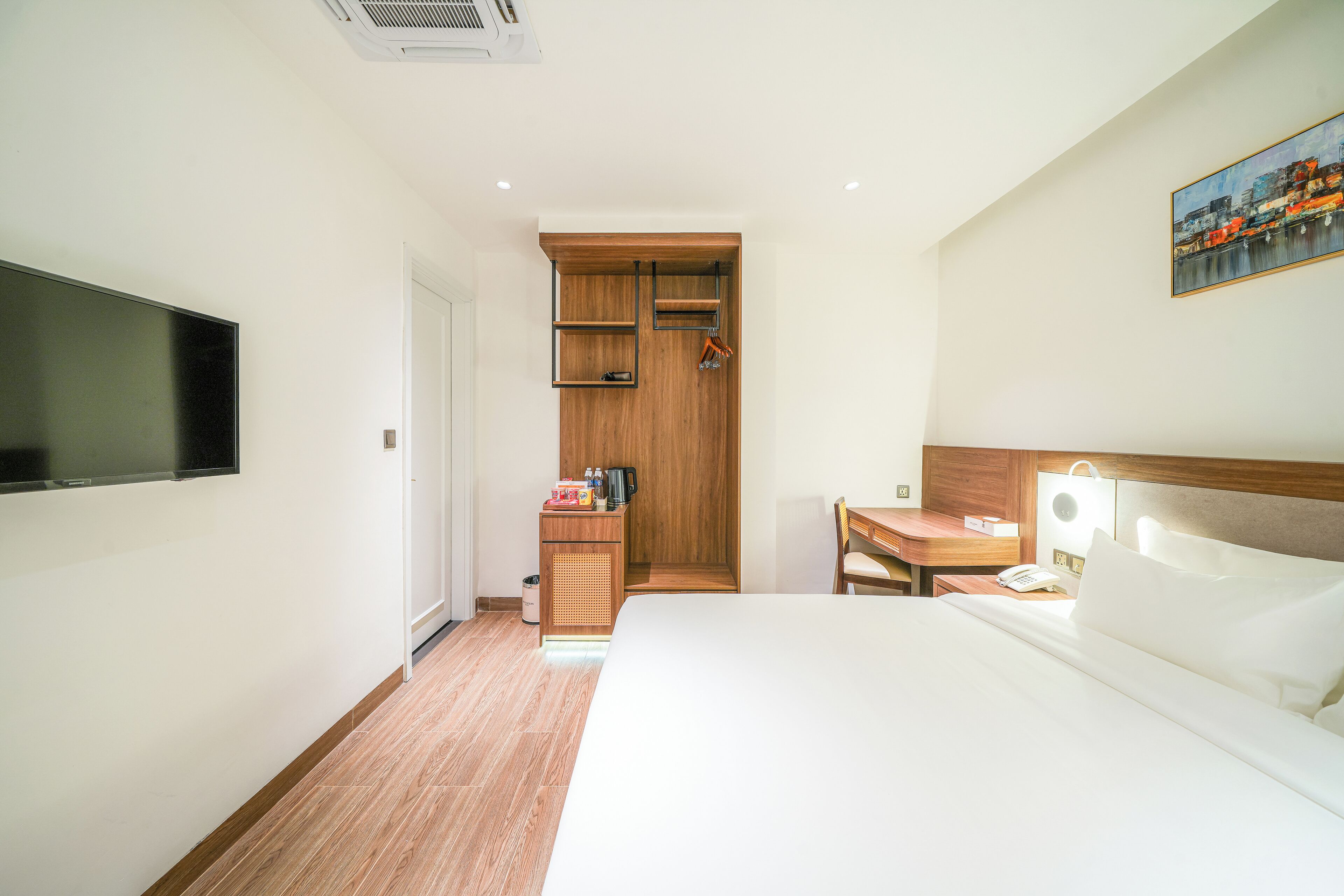Hotelkamer met een bed, een bureau, een televisie, een houten garderobe en een schilderij aan de muur.