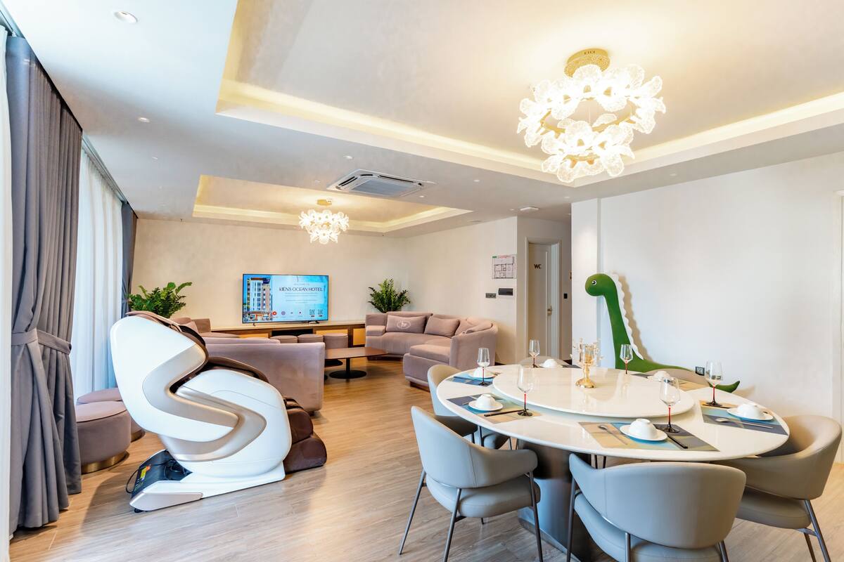Une chambre d’hôtel moderne dotée d’un coin repas, d’un fauteuil massant, d’un téléviseur à écran plat et d’une décoration sur le thème d’un dinosaure vert.