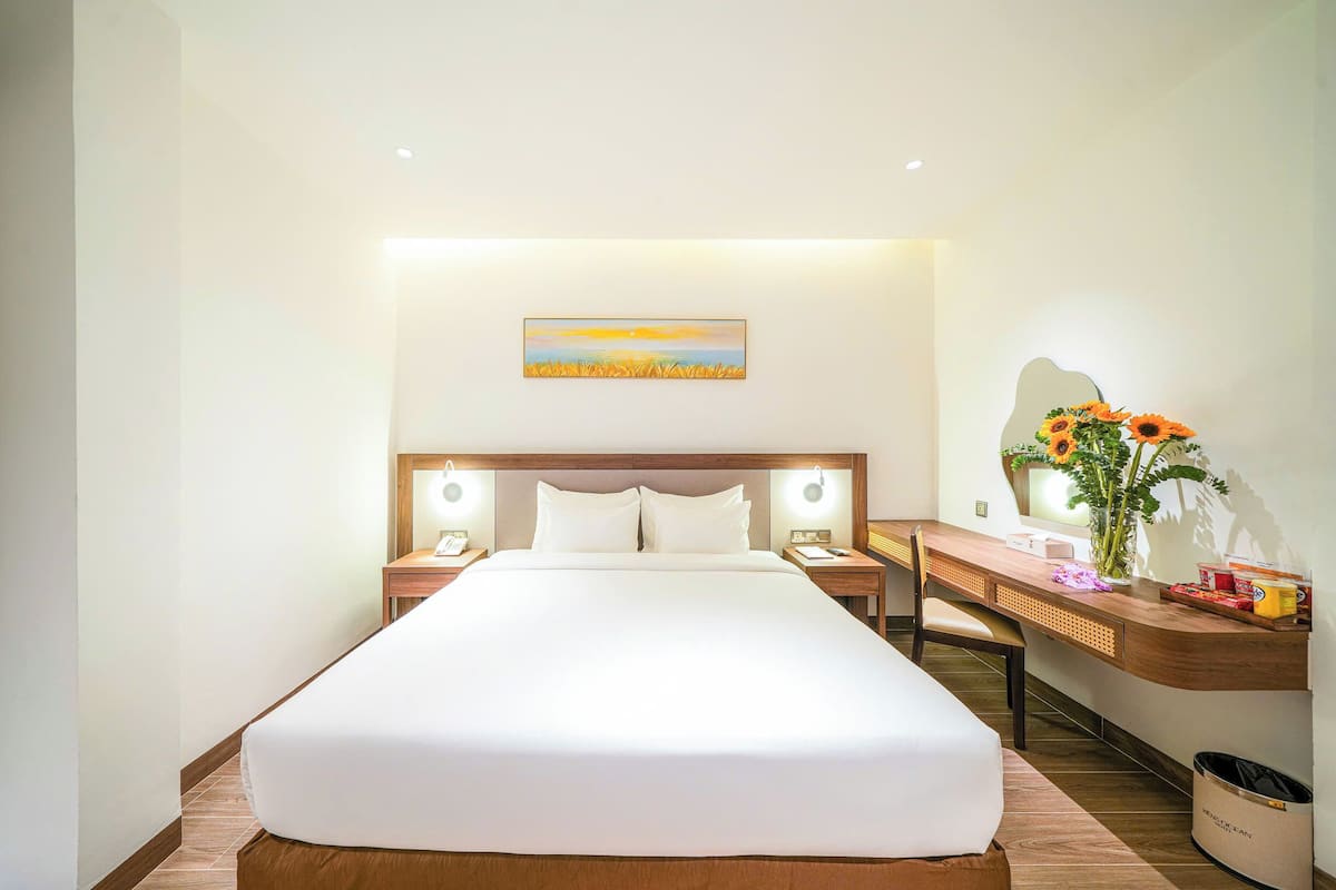 Une chambre d’hôtel avec un grand lit, des tables de chevet avec des lampes, un bureau avec une chaise et un tableau accroché au mur.
